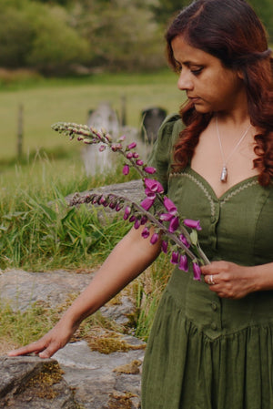 Woman in a green dress holding flowers in a cemetery with mountains in the background