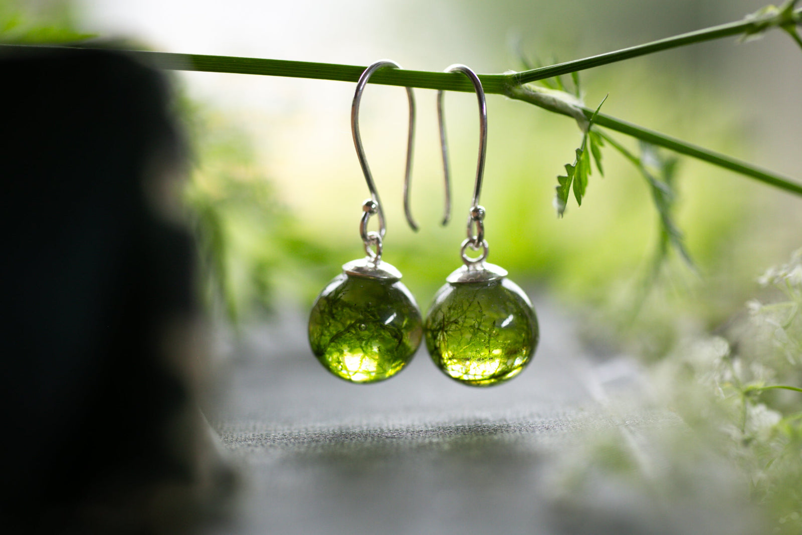 Green forest moss resin earrings on a branch with a blurred natural background